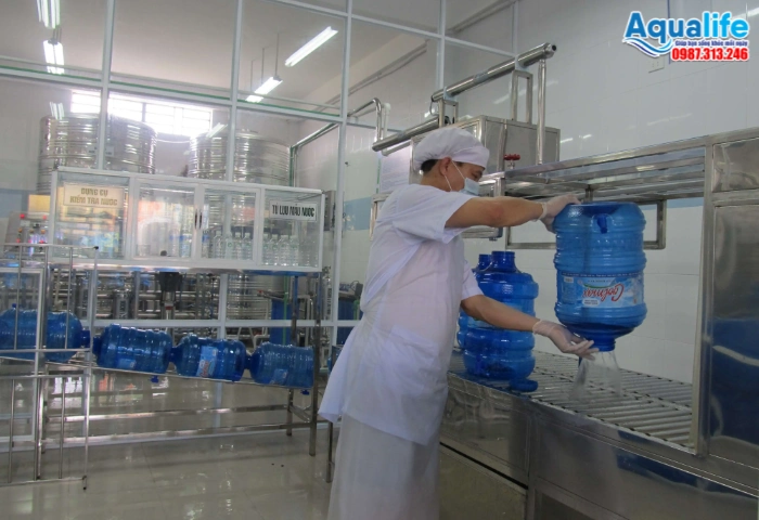 Nhân viên thao tác sục rửa và đưa bình nước 20L vào buồng chiết rót vô trùng
